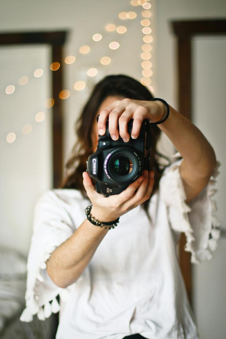 Photographer holding a camera to her eye in front of warm string lights
