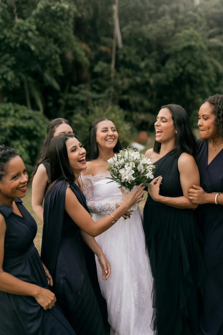 Bride laughing with her bridesmaids outdoors, holding a white bouquet
