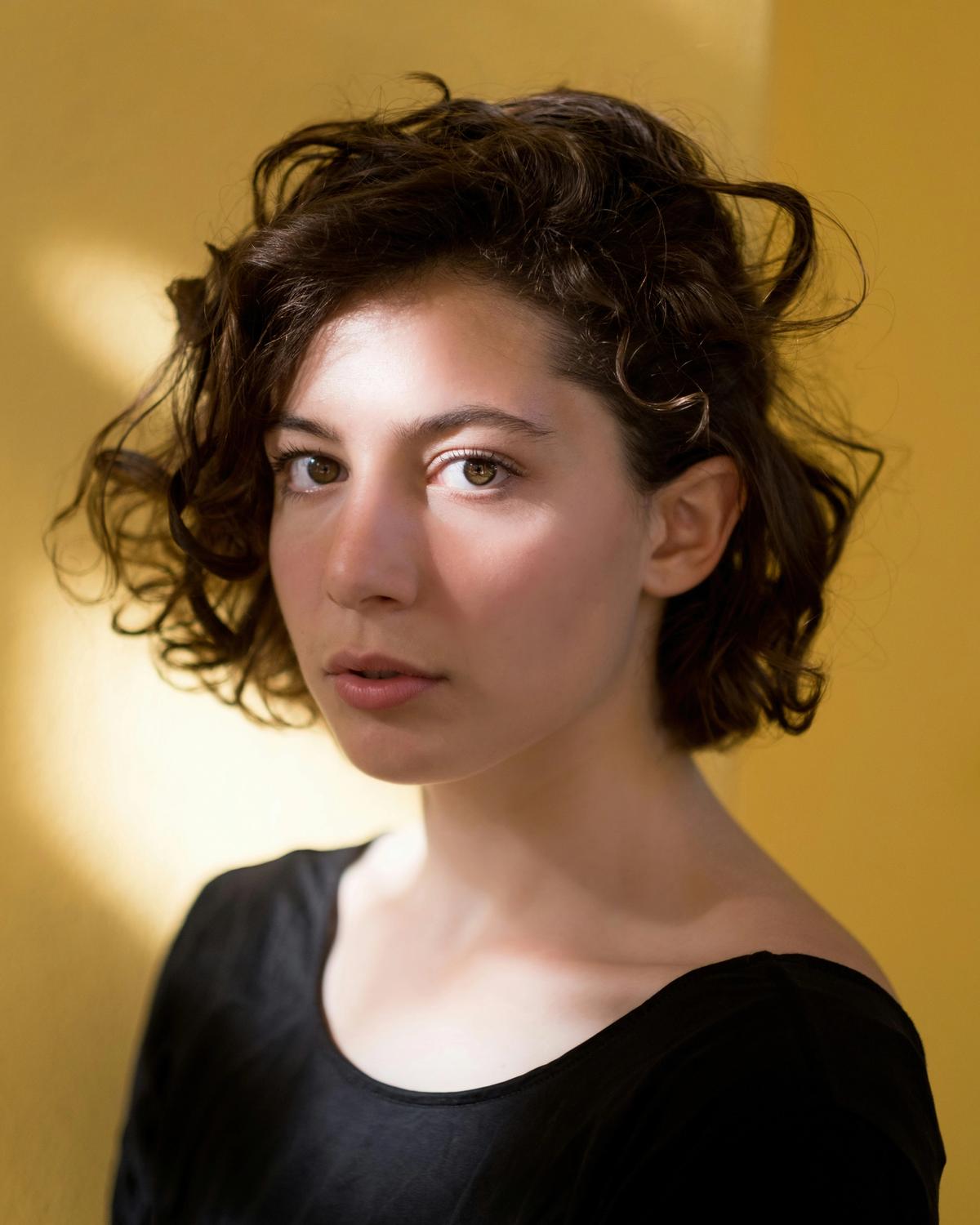 Portrait of a woman with short curly hair against a yellow wall