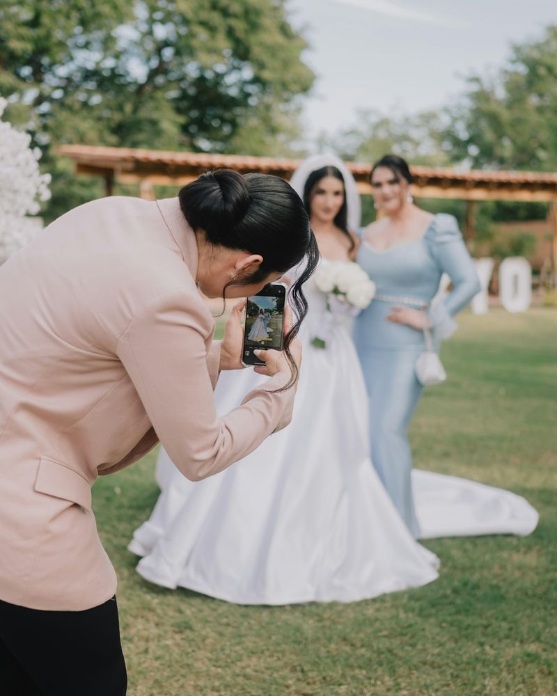 Photographer crouching to photograph a bride and her bridesmaid on a lawn