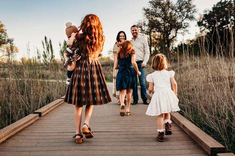 Family walking a boardwalk through tall grass at golden hour