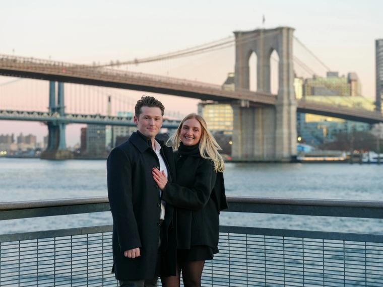 Engaged couple by the water with the Brooklyn Bridge behind them