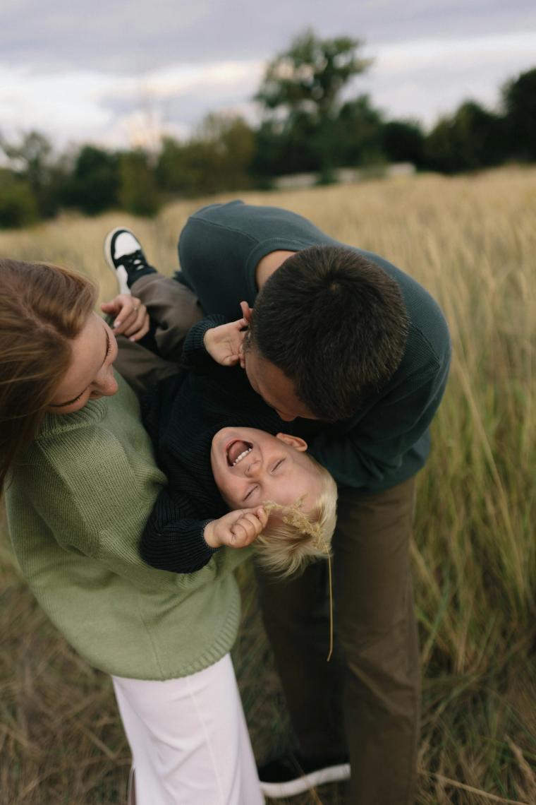 Parents playing with their laughing child in a grassy field