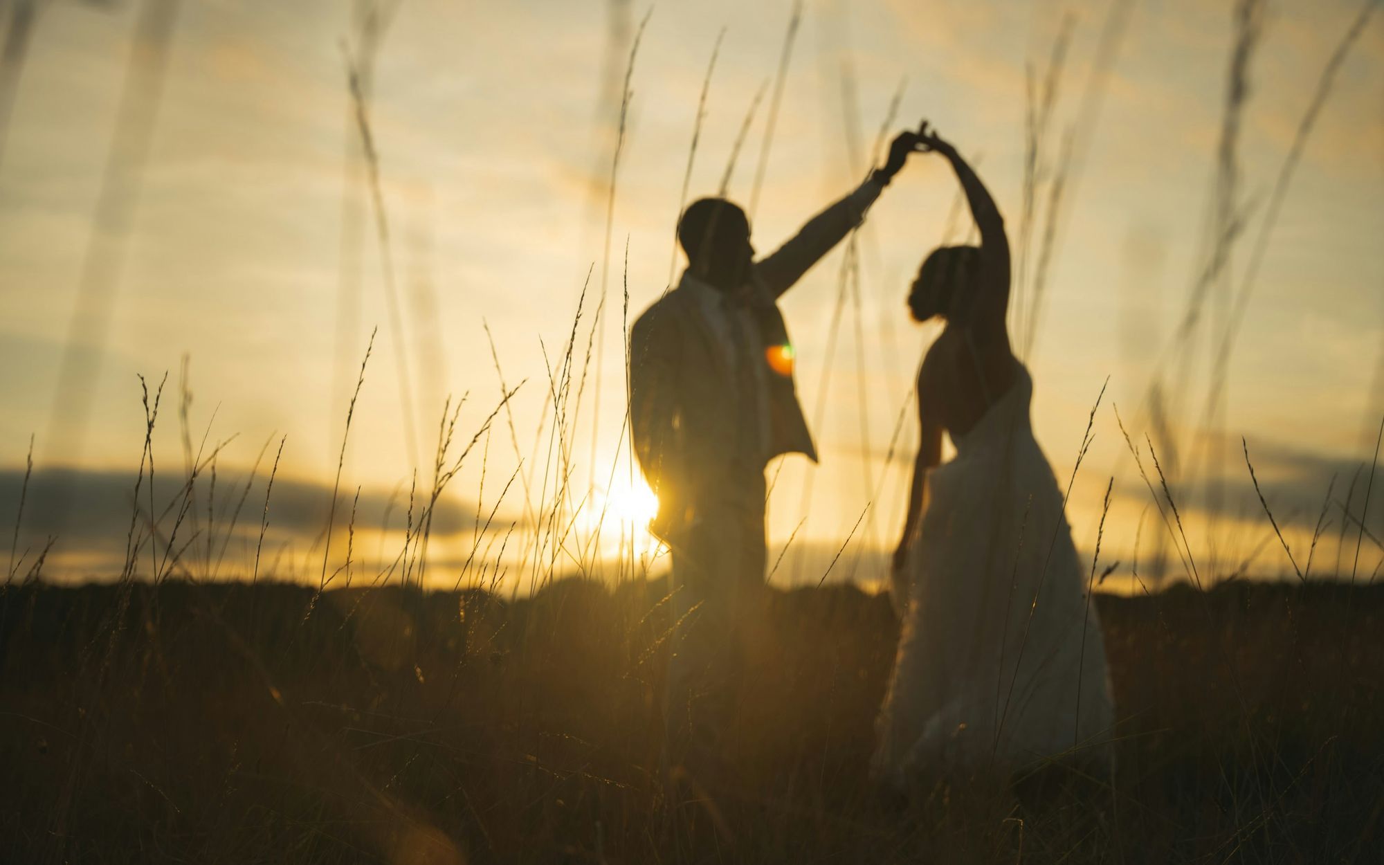 Bride and groom dancing in silhouette in a field at sunset