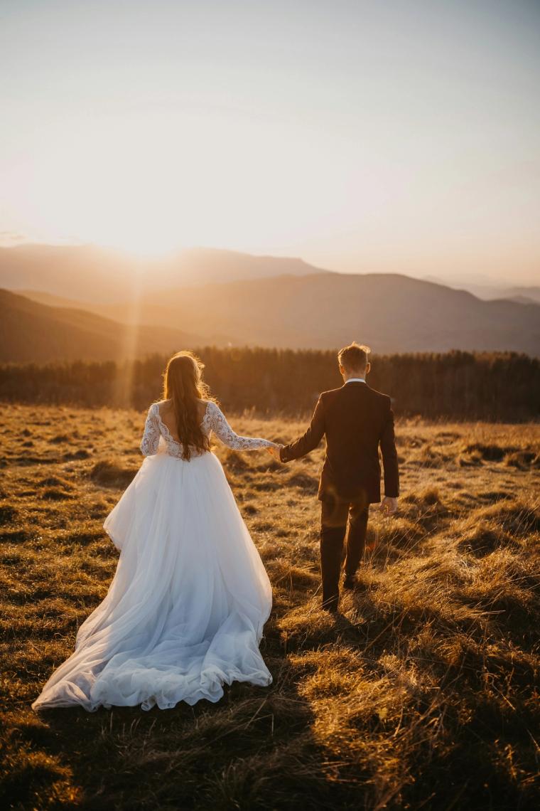 Bride and groom walking hand in hand across a mountain meadow at golden hour