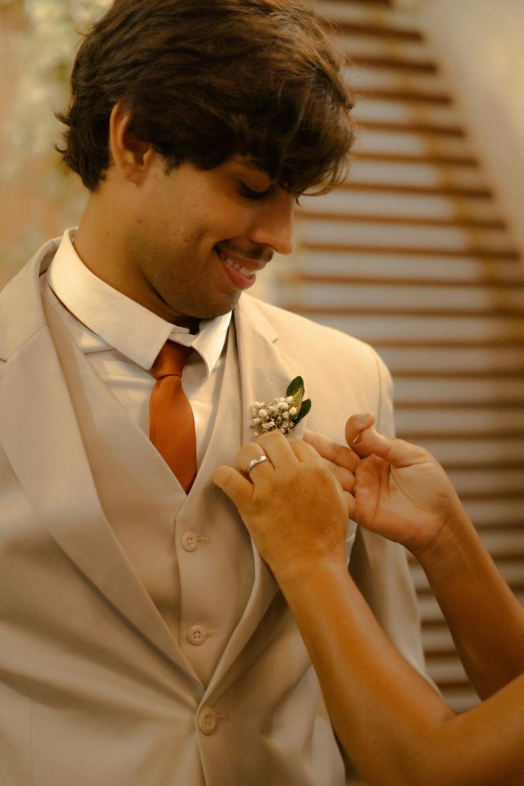 Groom smiling while his boutonniere is pinned on
