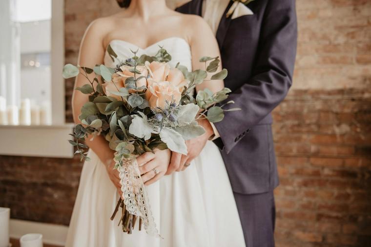 Bride holding a peach and eucalyptus bouquet beside the groom
