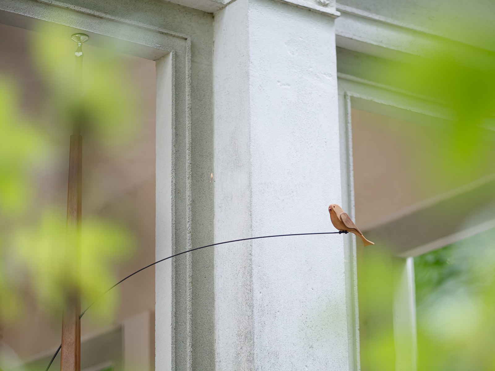 Boga by NOEMAR — tensioned floor-to-ceiling sculpture installed in a Viennese interior, with a small bird perched at the end of its branch.