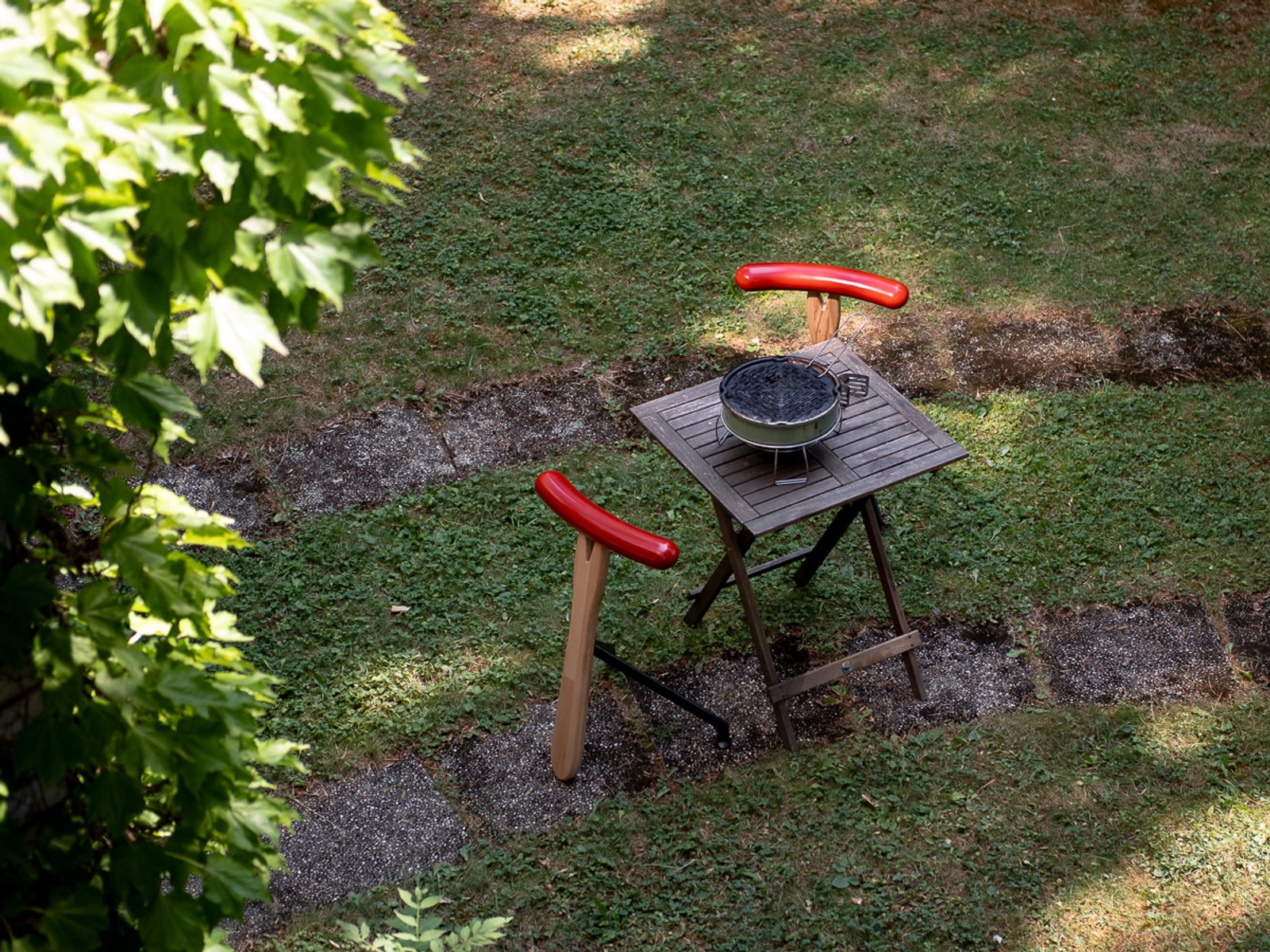 Würstelhocker by NOEMAR — sausage-shaped stool balanced on a wooden fork base. Wiener Norm collection, 2026 (view 3 of 9).