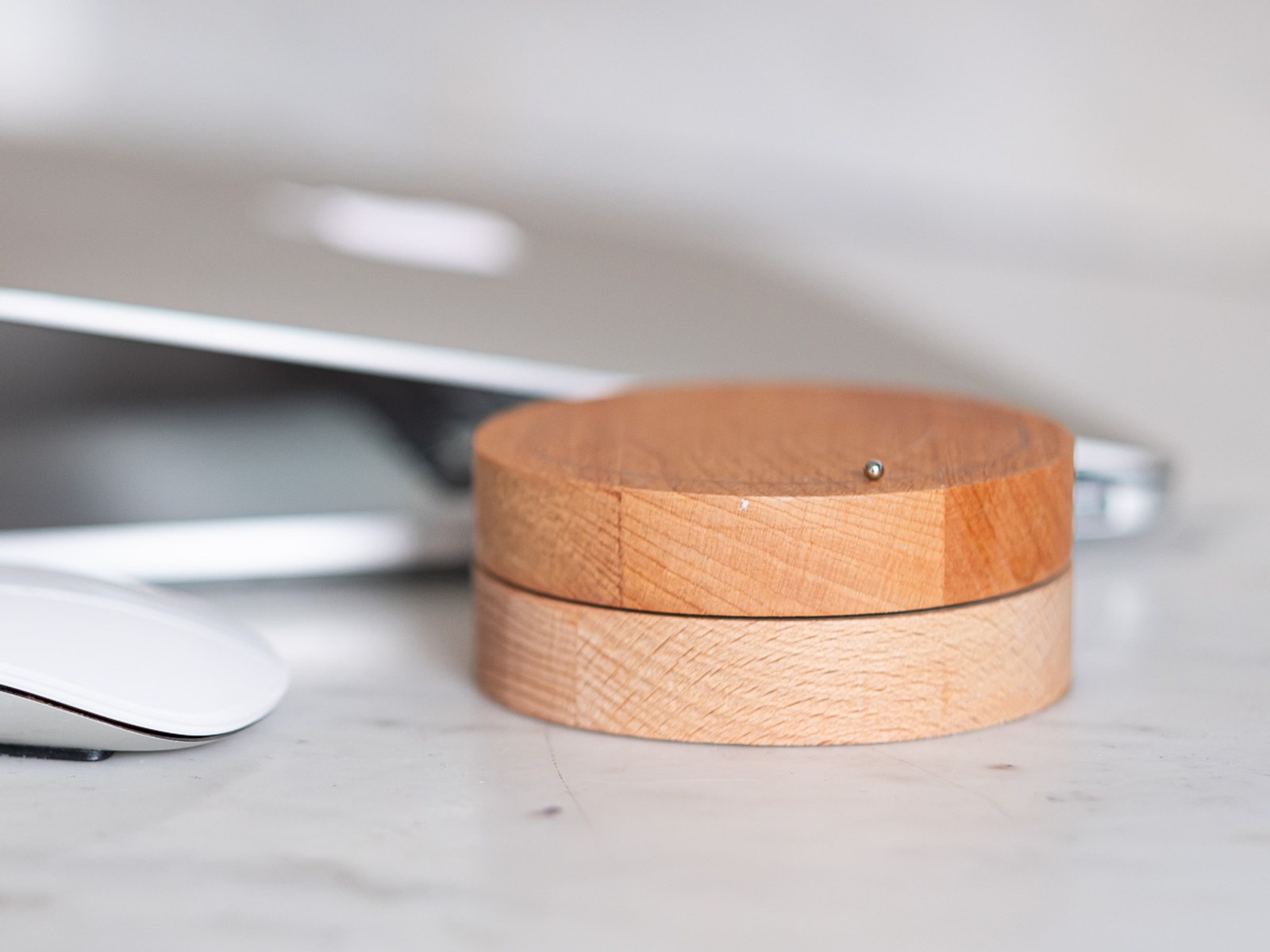 Toki by NOEMAR — side view of the layered wooden disc on a marble desk, with a laptop and mouse in the background.