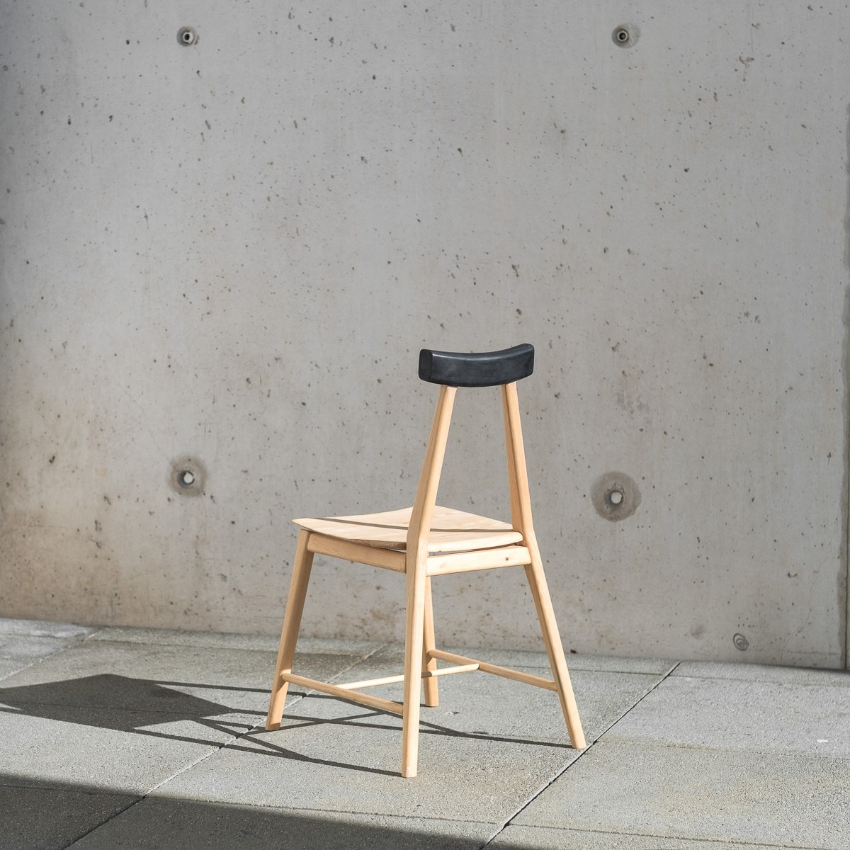 Ryoku by NOEMAR — a light wooden chair with a black cast rubber backrest piece slotted onto its two rear legs.