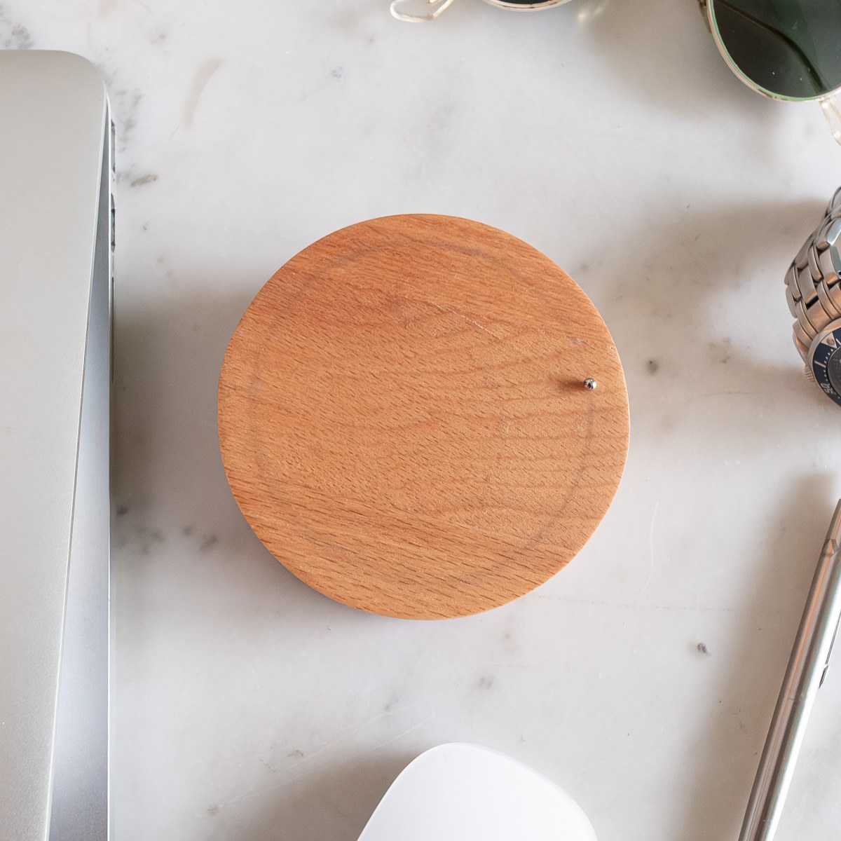 Toki by NOEMAR — the wooden disc and steel ball seen from above on a marble desk, beside a laptop, watch, and sunglasses.