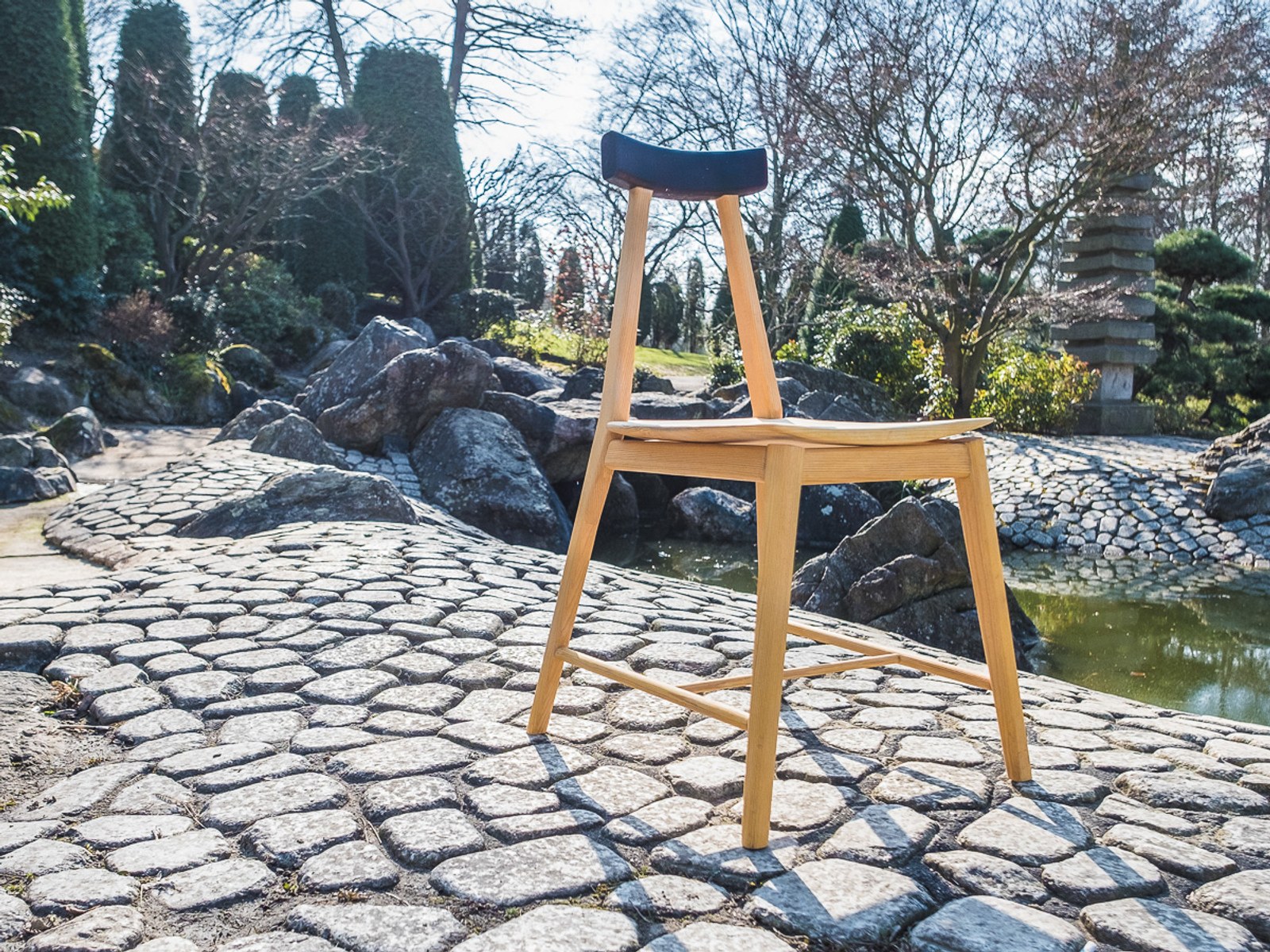 Ryoku — the chair set on a stone path in a Japanese garden, beside a pond and stone lantern.