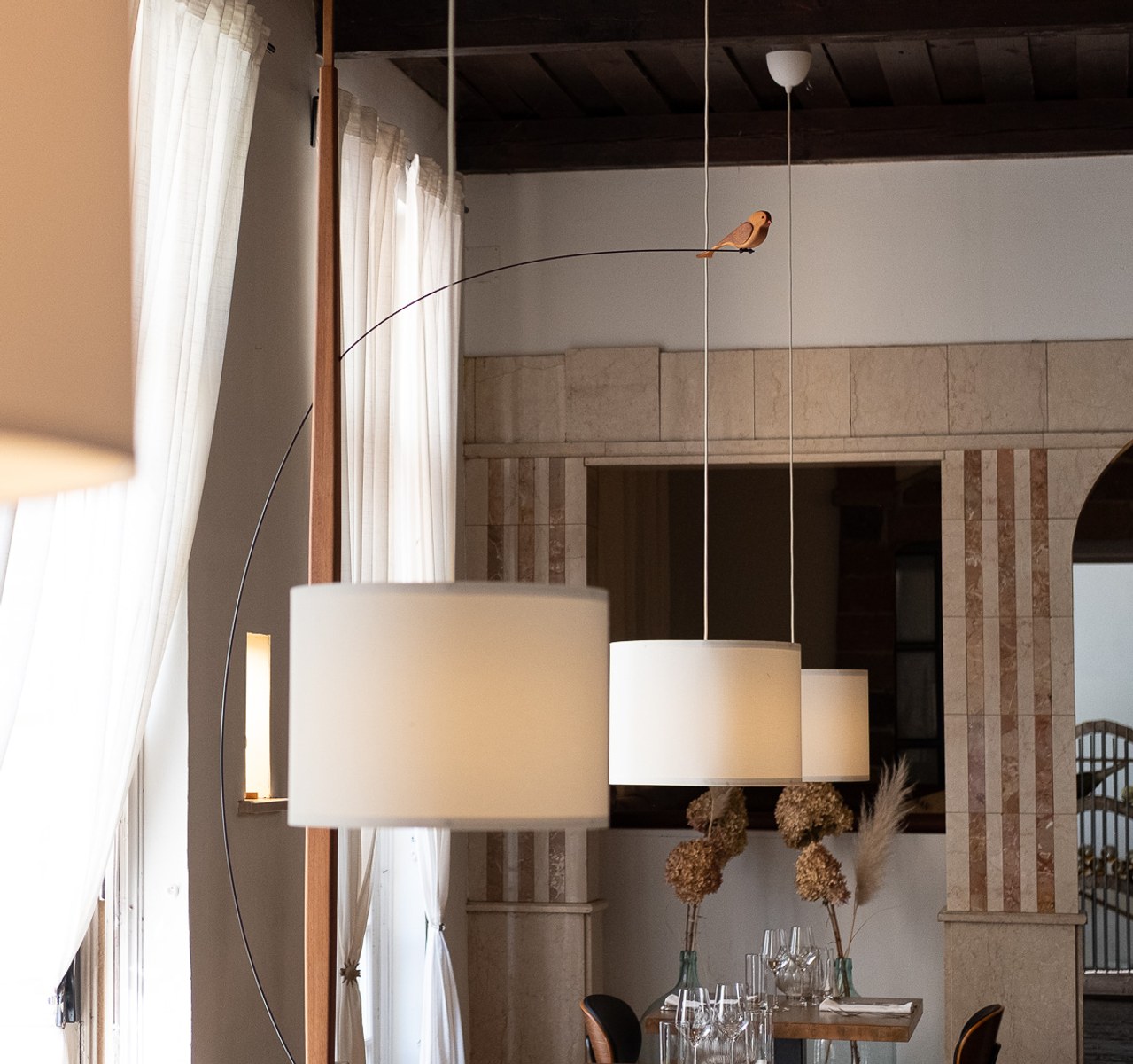 Boga by NOEMAR — tensioned floor-to-ceiling sculpture with a small bird perched at the end of its branch. Wiener Norm collection, 2026 (view 4 of 7).