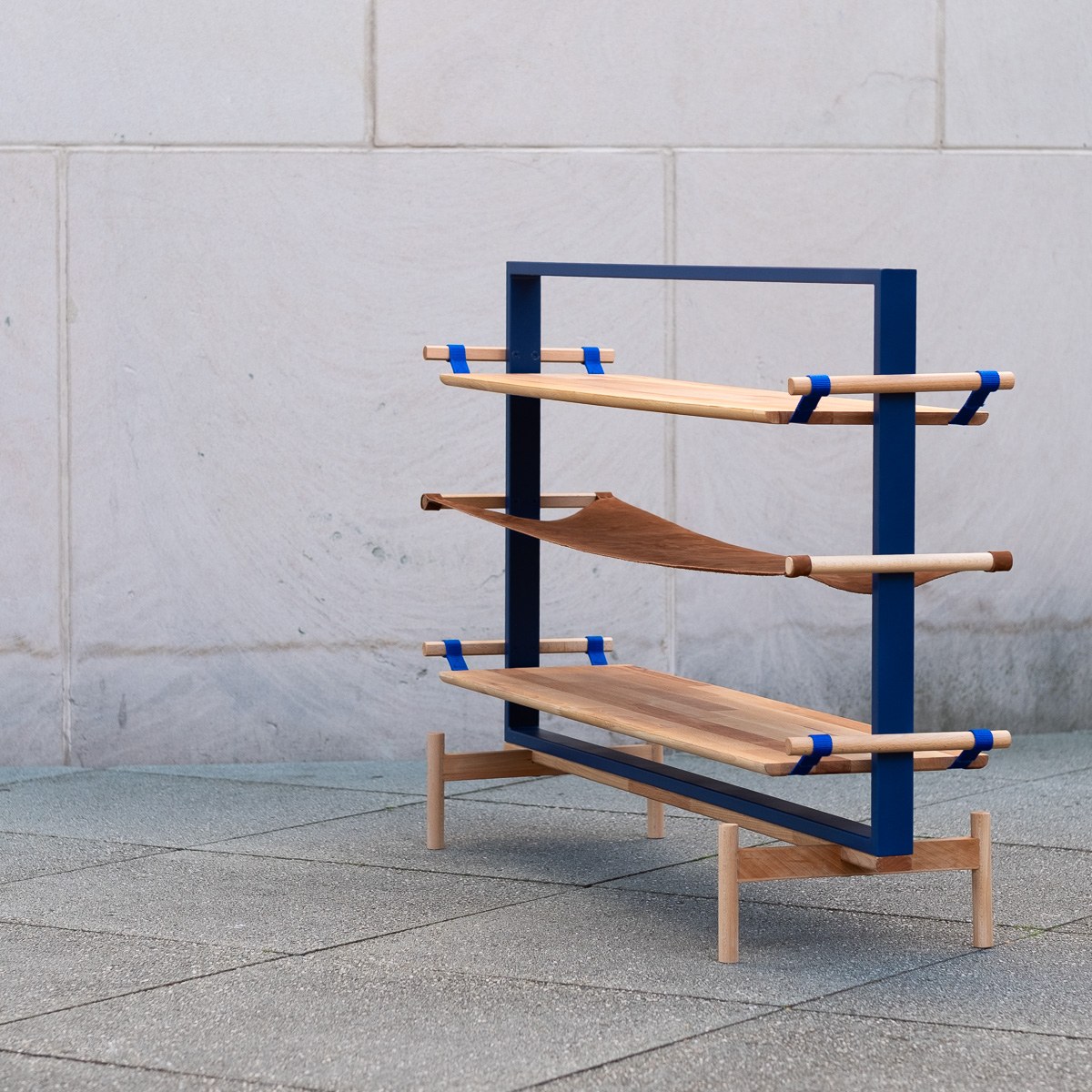 Tendere by NOEMAR — a modular blue steel shelf frame holding wood boards suspended by tensioned polypropylene webbing straps.
