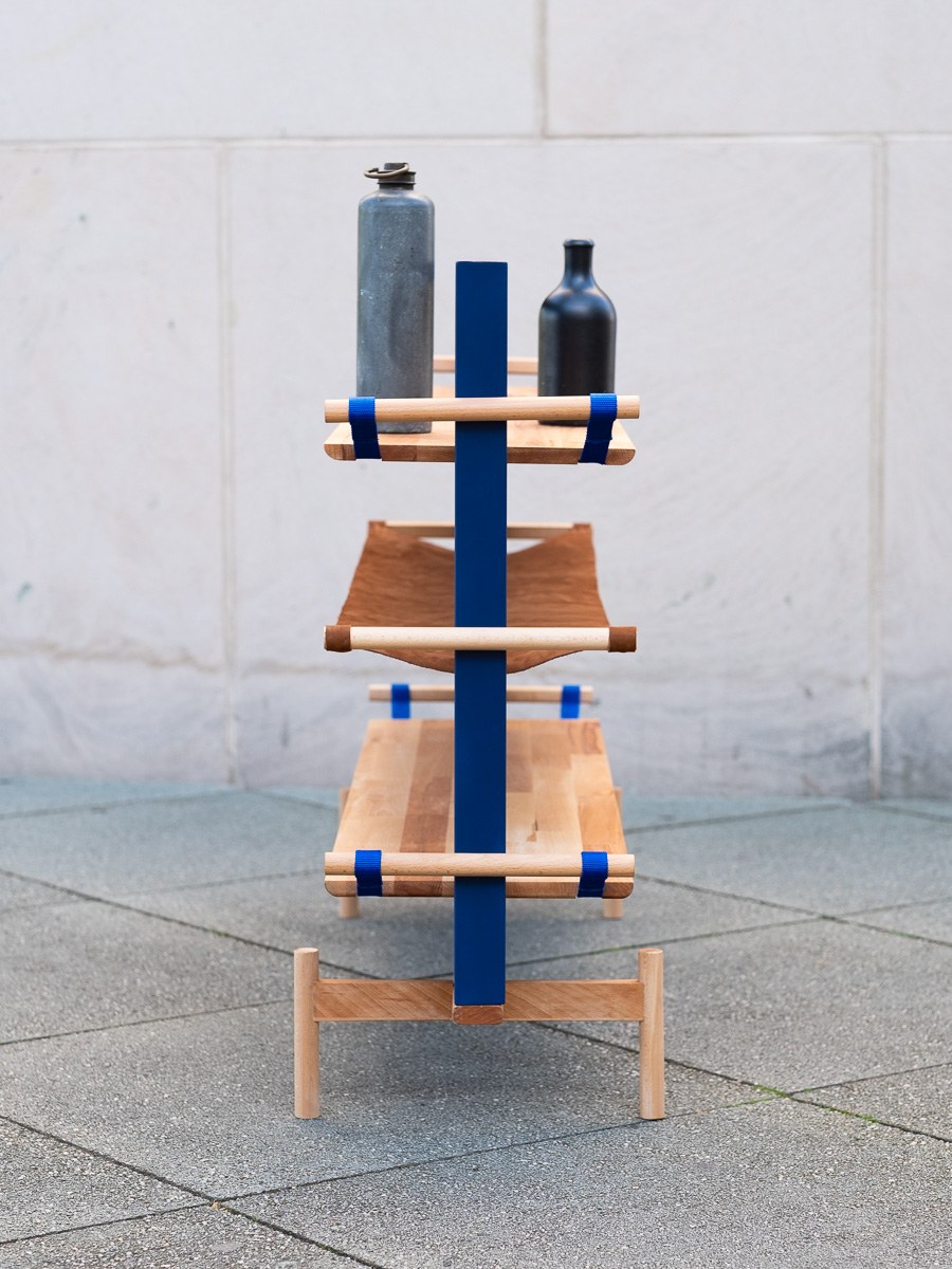Tendere — frontal detail with bottles on the top shelf and the leather sling below.