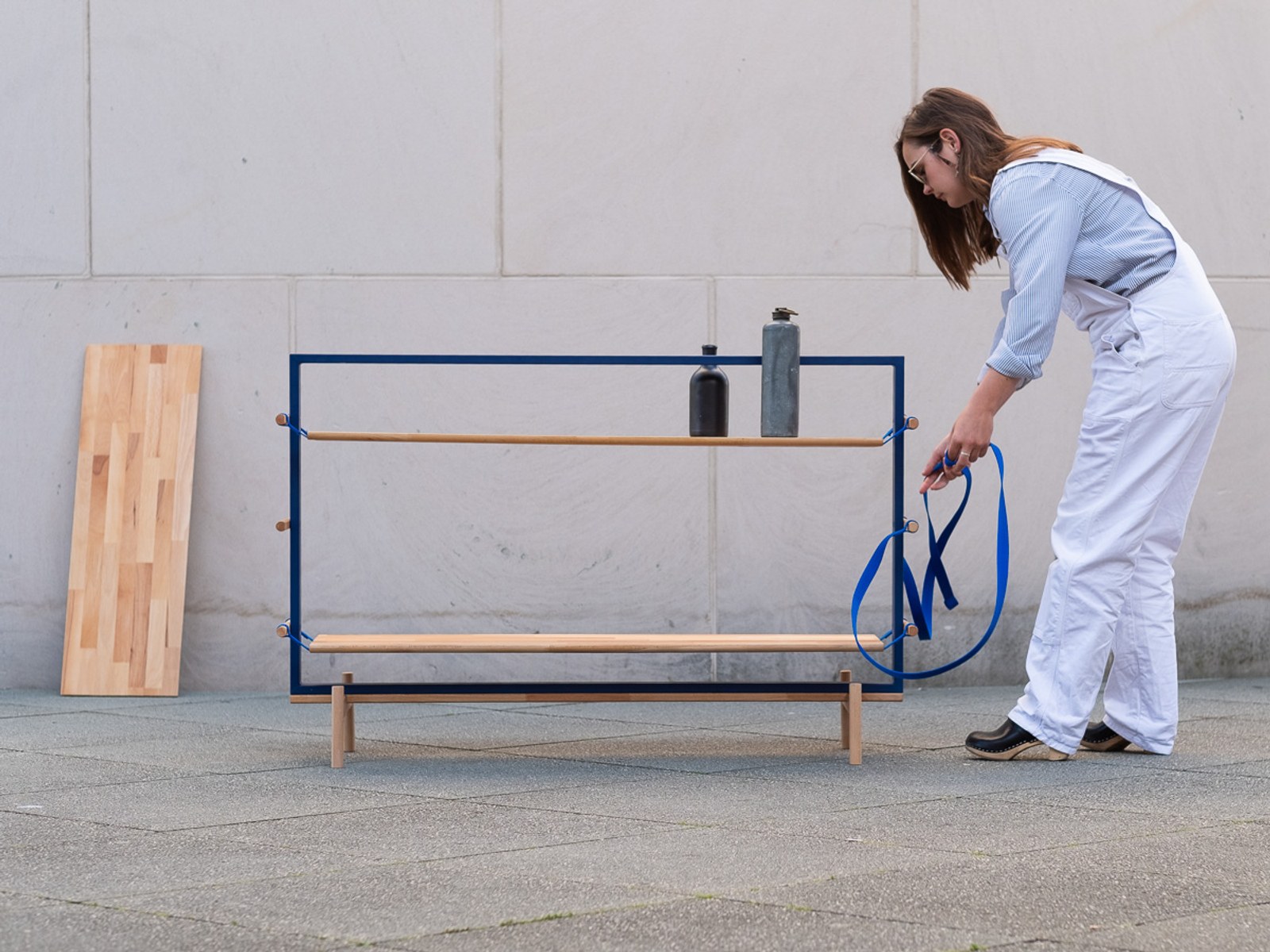 Tendere — a hand holding a webbing strap beside a spare board leaning against the wall.