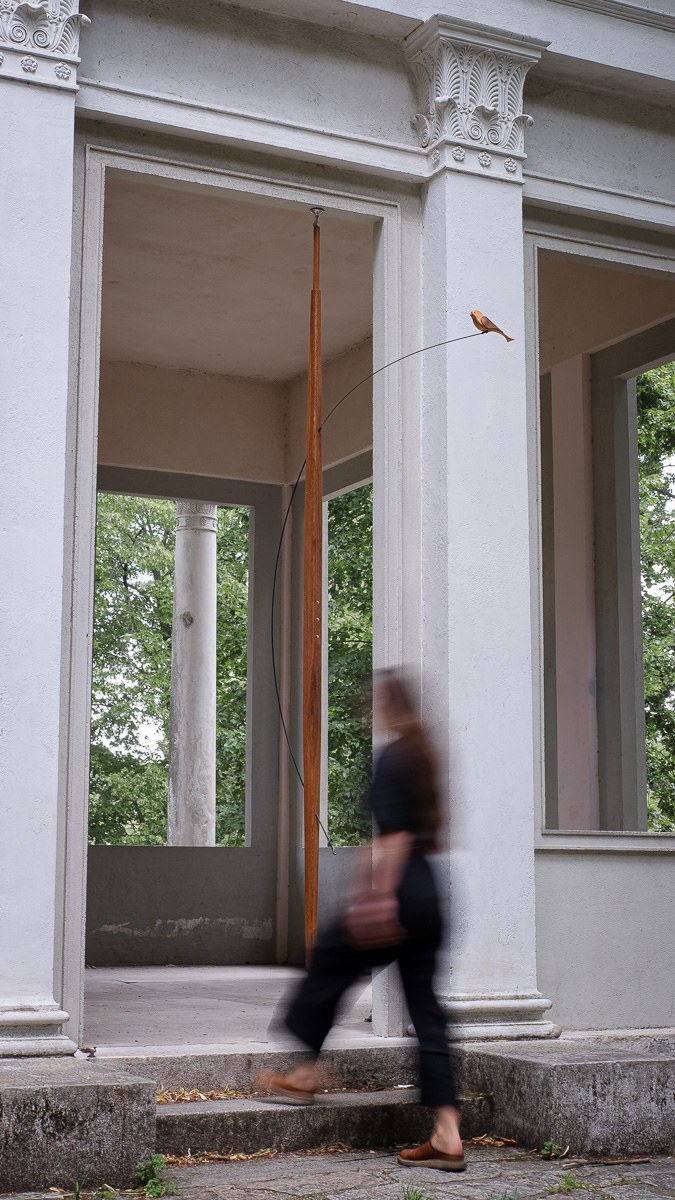 Boga by NOEMAR — tensioned floor-to-ceiling sculpture with a small bird perched at the end of its branch. Wiener Norm collection, 2026 