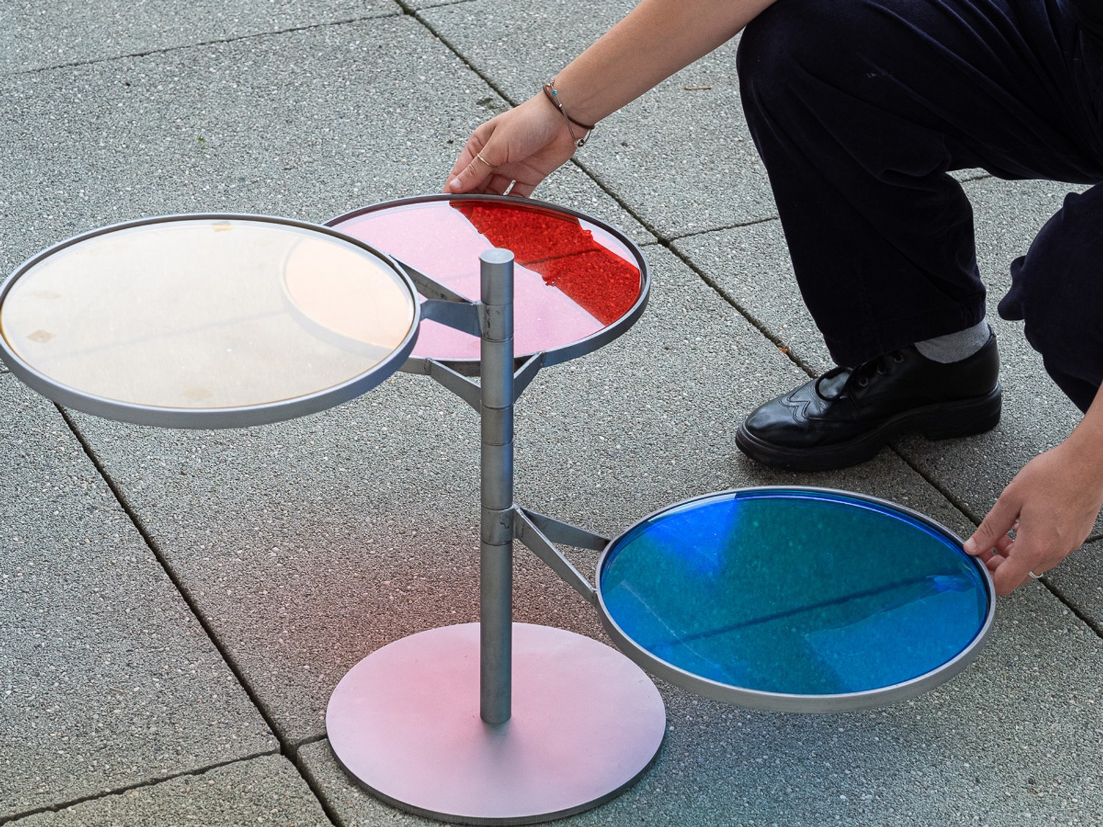 FLTR by NOEMAR — a person adjusting the red and blue discs, their coloured light reflecting on the pavement.