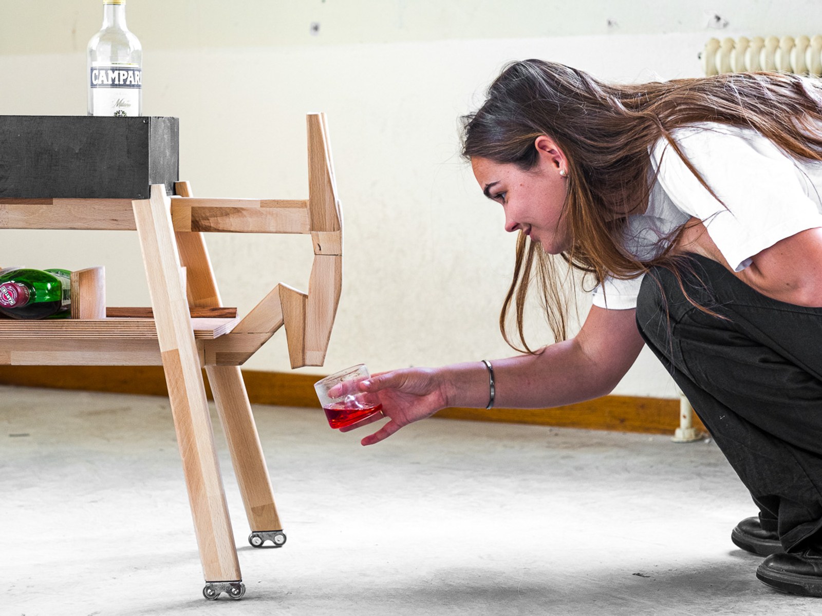 Donkey by NOEMAR — a person reaching for a Campari drink resting on one of the stool legs.