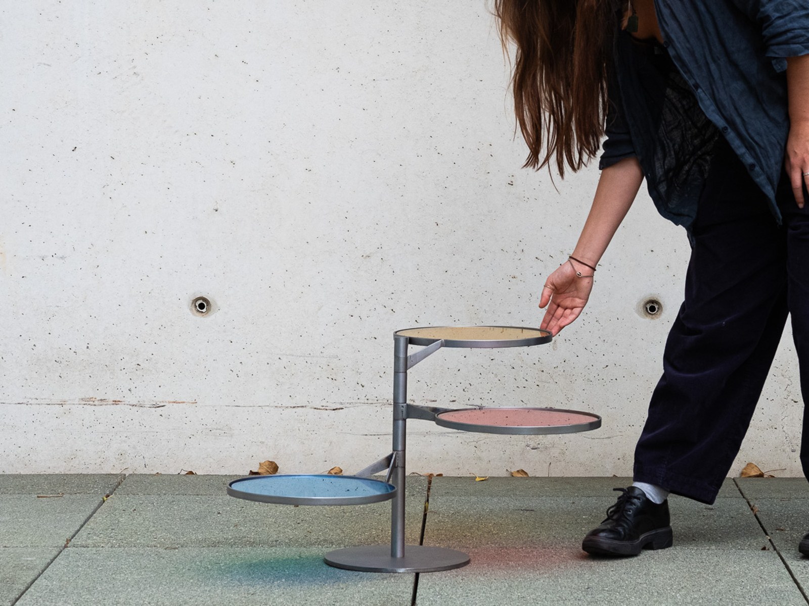 FLTR by NOEMAR — a person reaching to tilt one of the discs against a concrete wall.