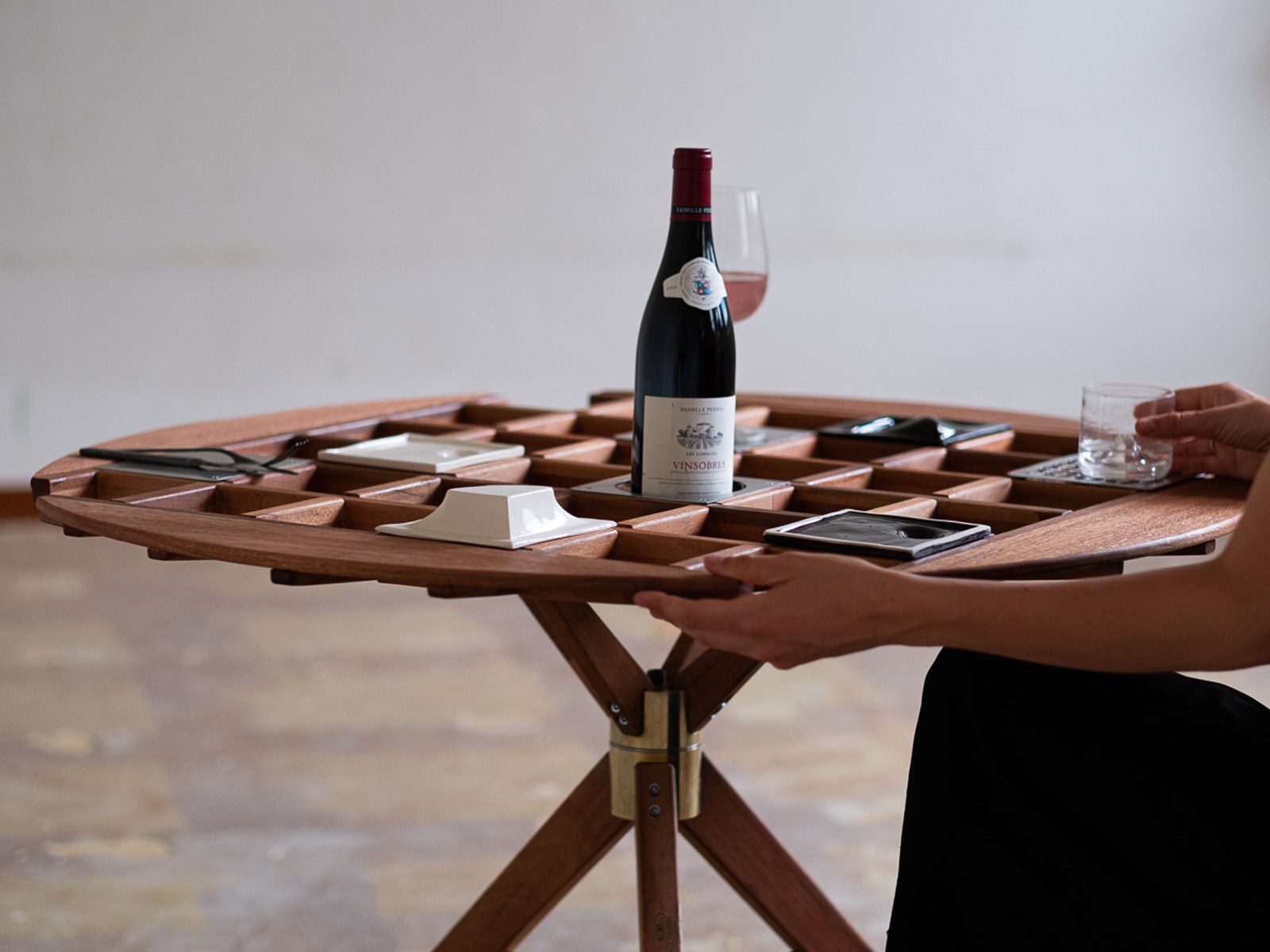 An Audience of Me — detail of the grid surface with a wine bottle, glass, and ceramic dishes set into the cells.
