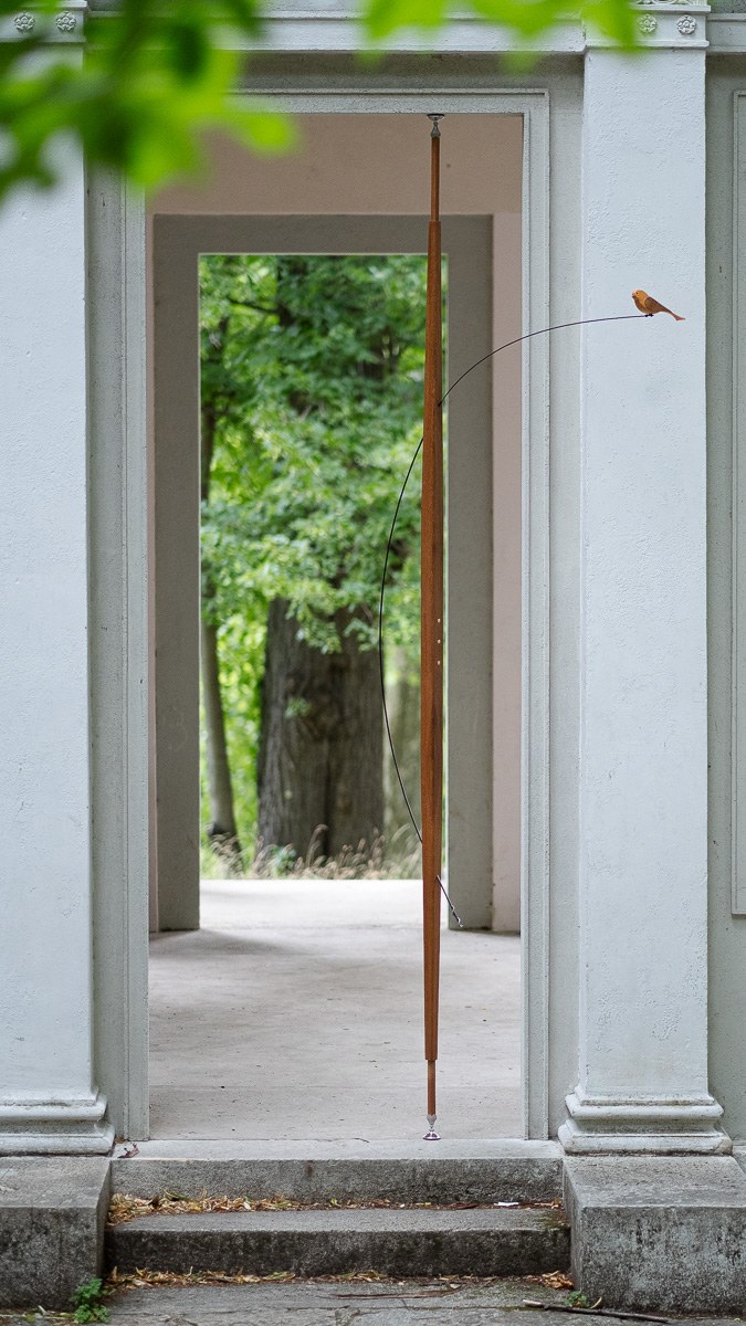 Boga by NOEMAR — tensioned floor-to-ceiling sculpture with a small bird perched at the end of its branch. Wiener Norm collection, 2026 