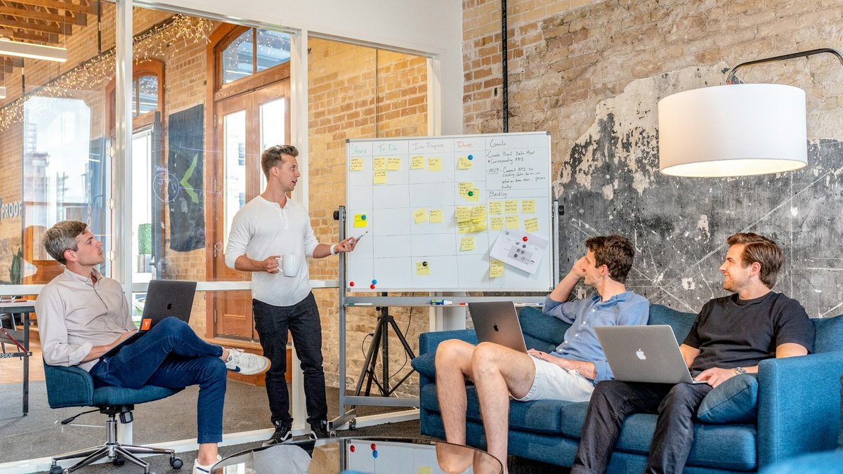 Team meeting in a loft office with a whiteboard full of notes and colleagues with laptops