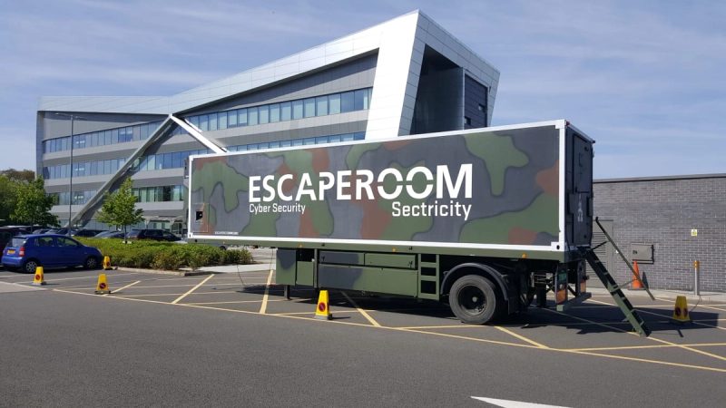 De Escape Truck van Sectricity, een oplegger in camouflageprint met het opschrift Escaperoom Cyber Security, geparkeerd voor een kantoorgebouw