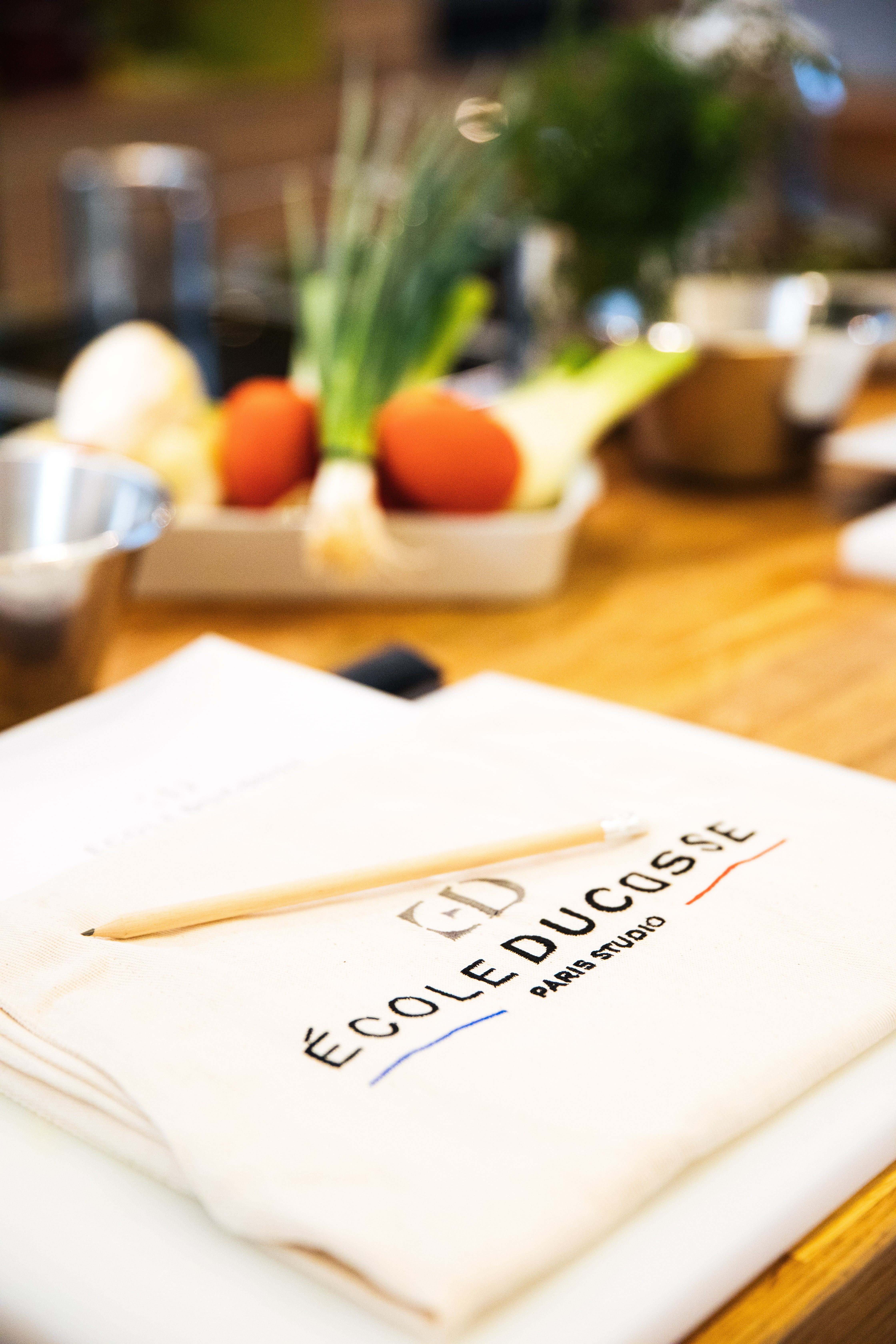 Tablier École Ducasse posé près de légumes frais