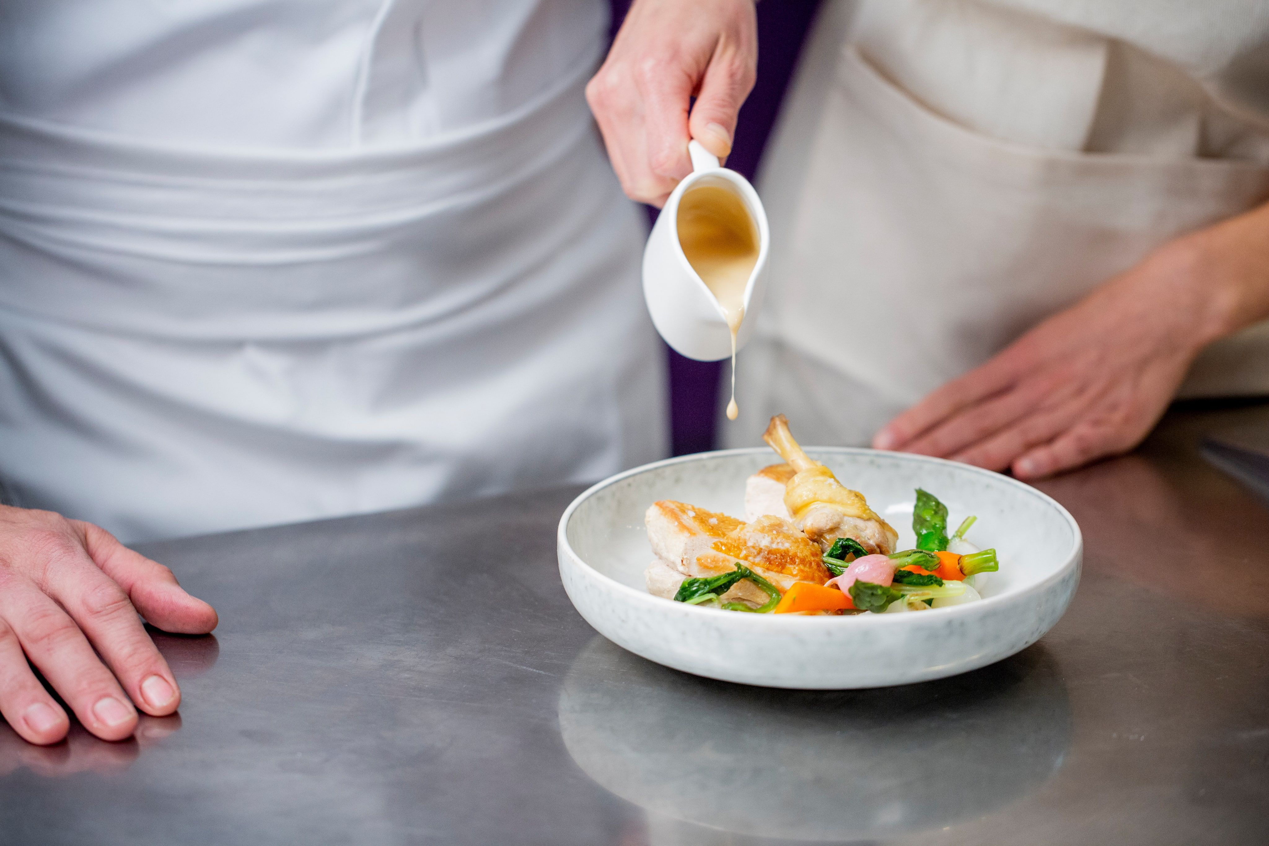 Chef versant un jus sur une volaille rôtie en assiette