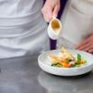Chef versant un jus sur une volaille rôtie en assiette