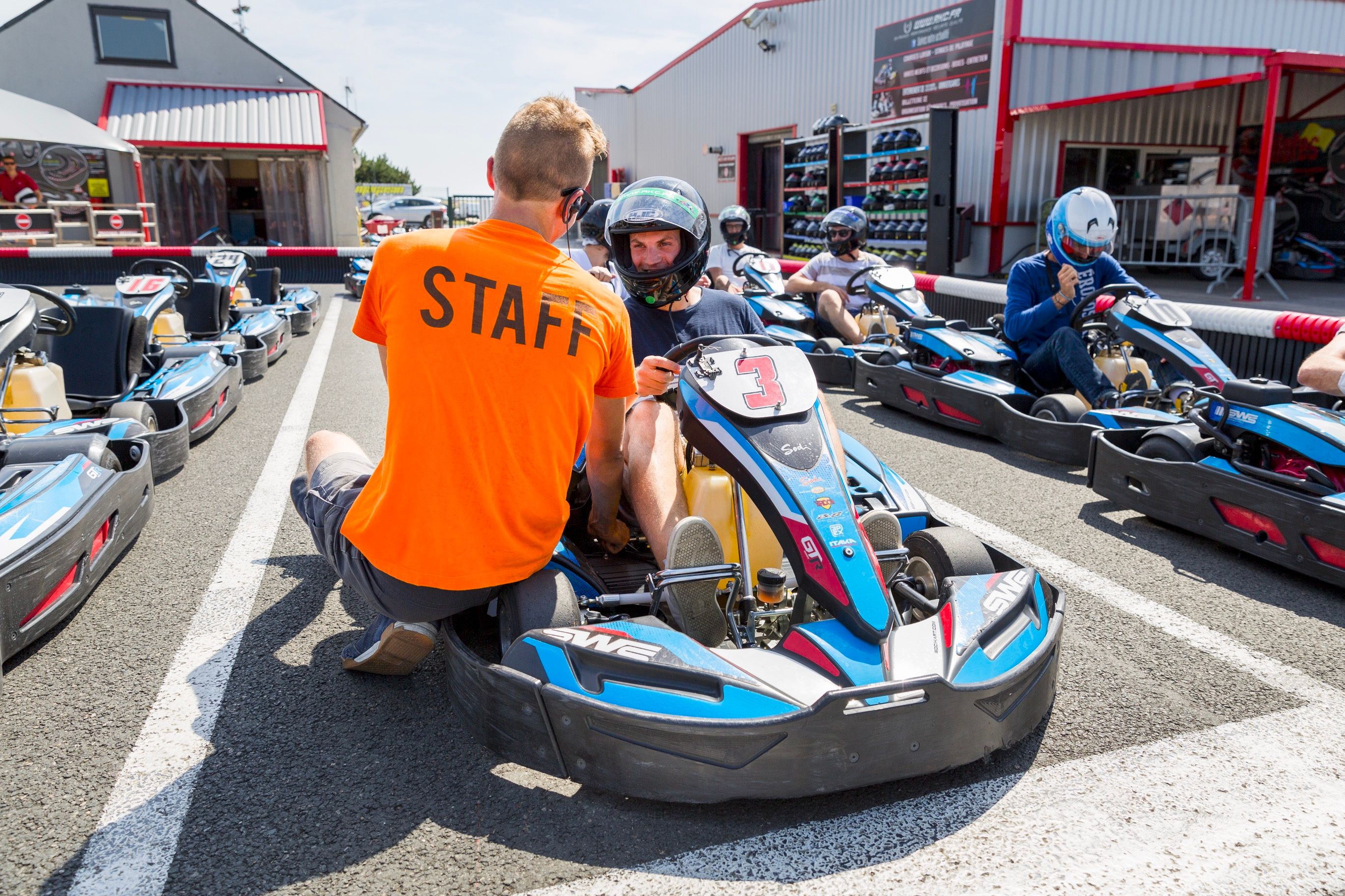 Briefing d'un pilote de karting par un encadrant en orange