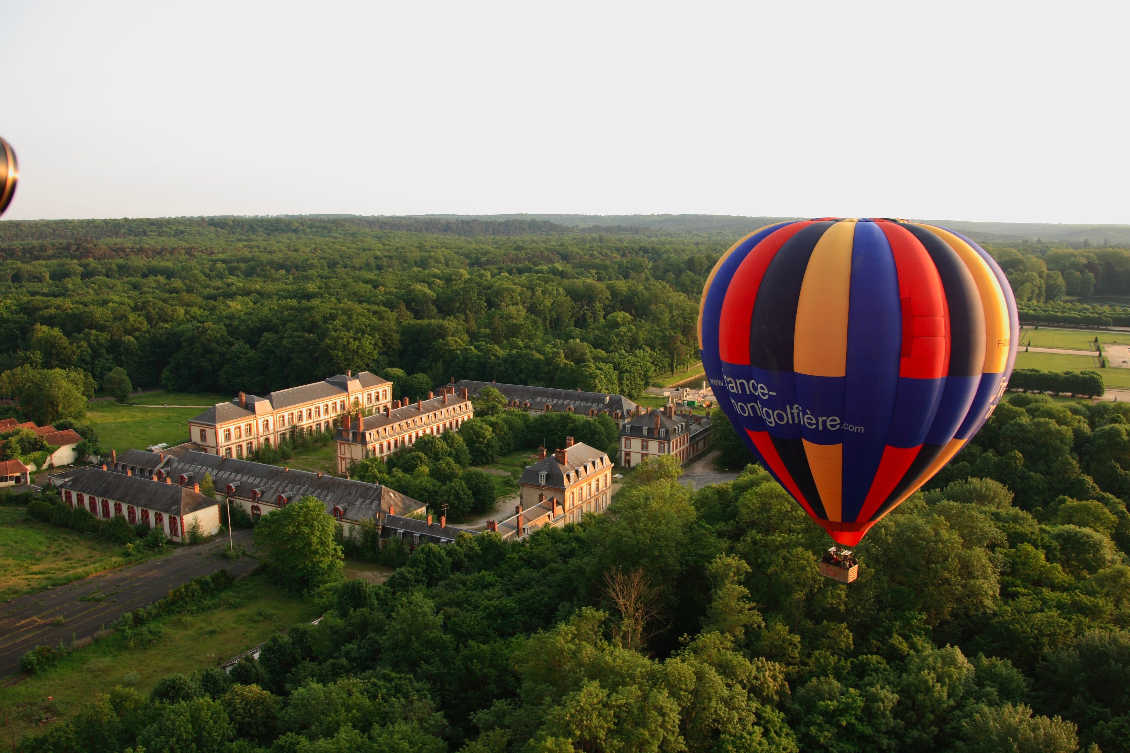 Montgolfière colorée survolant un château et sa forêt au lever du soleil