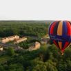 Montgolfière colorée survolant un château et sa forêt au lever du soleil