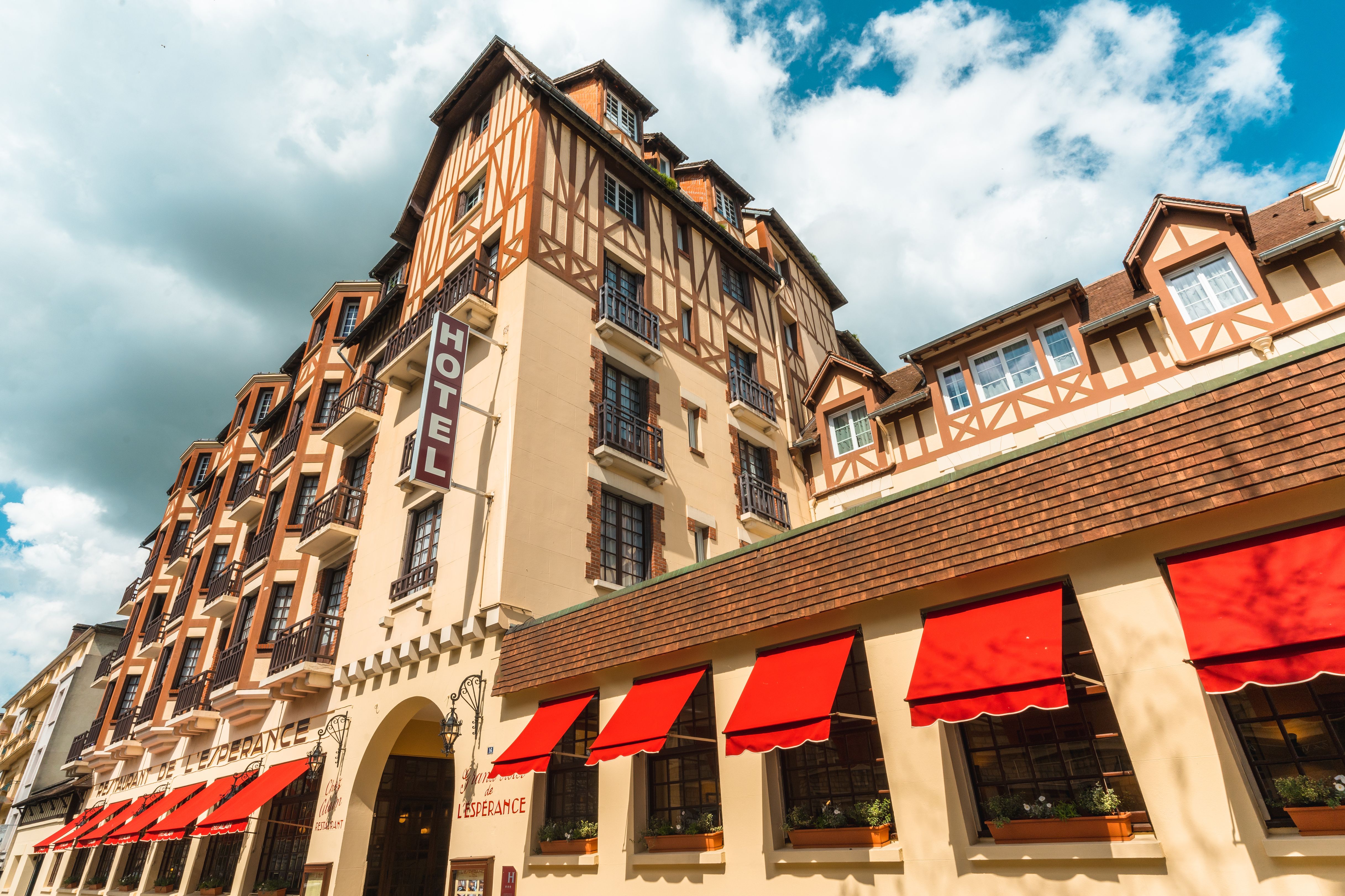 Façade à colombages de l'Hôtel L'Espérance avec stores rouges