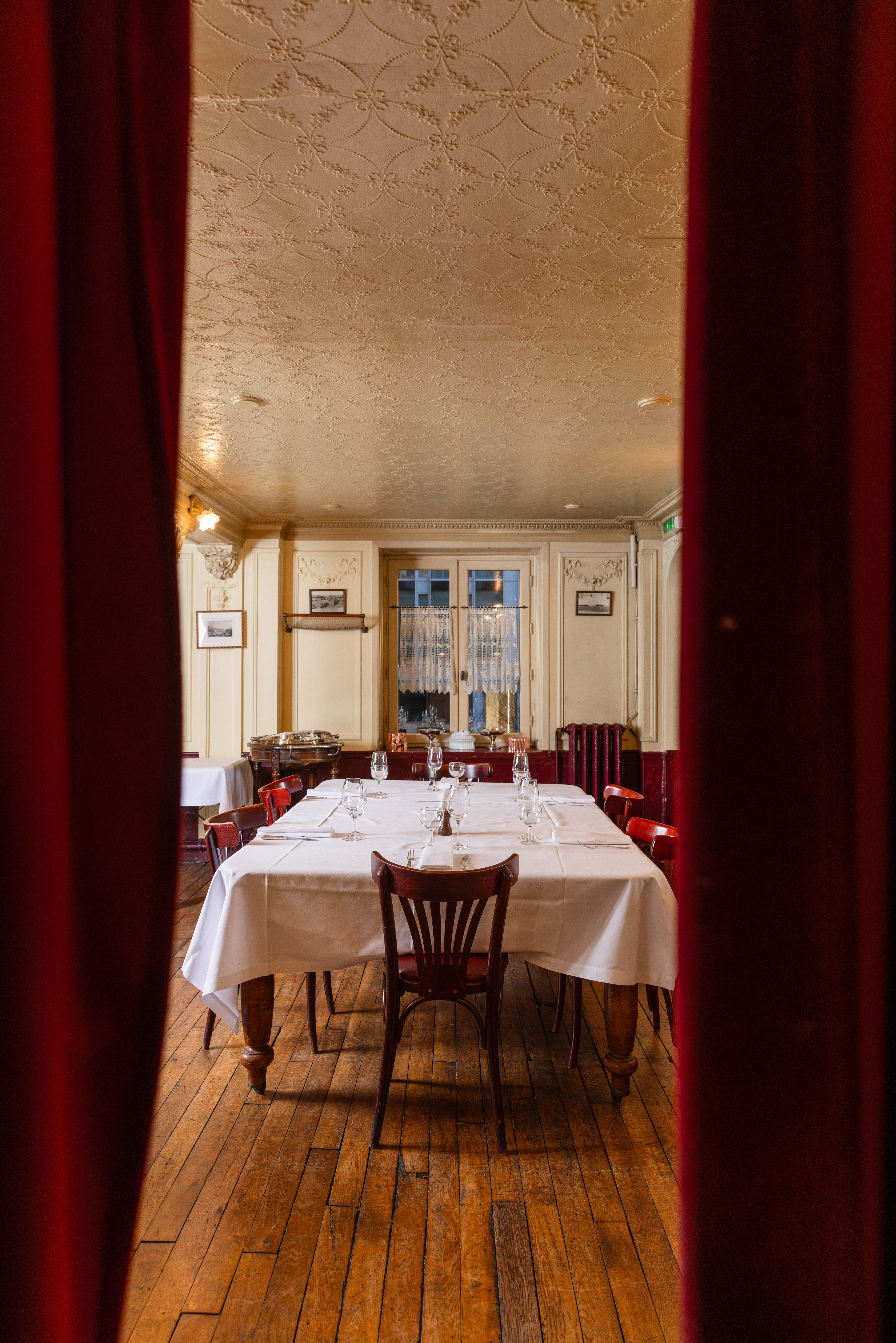 Petite salle de restaurant aperçue entre rideaux rouges