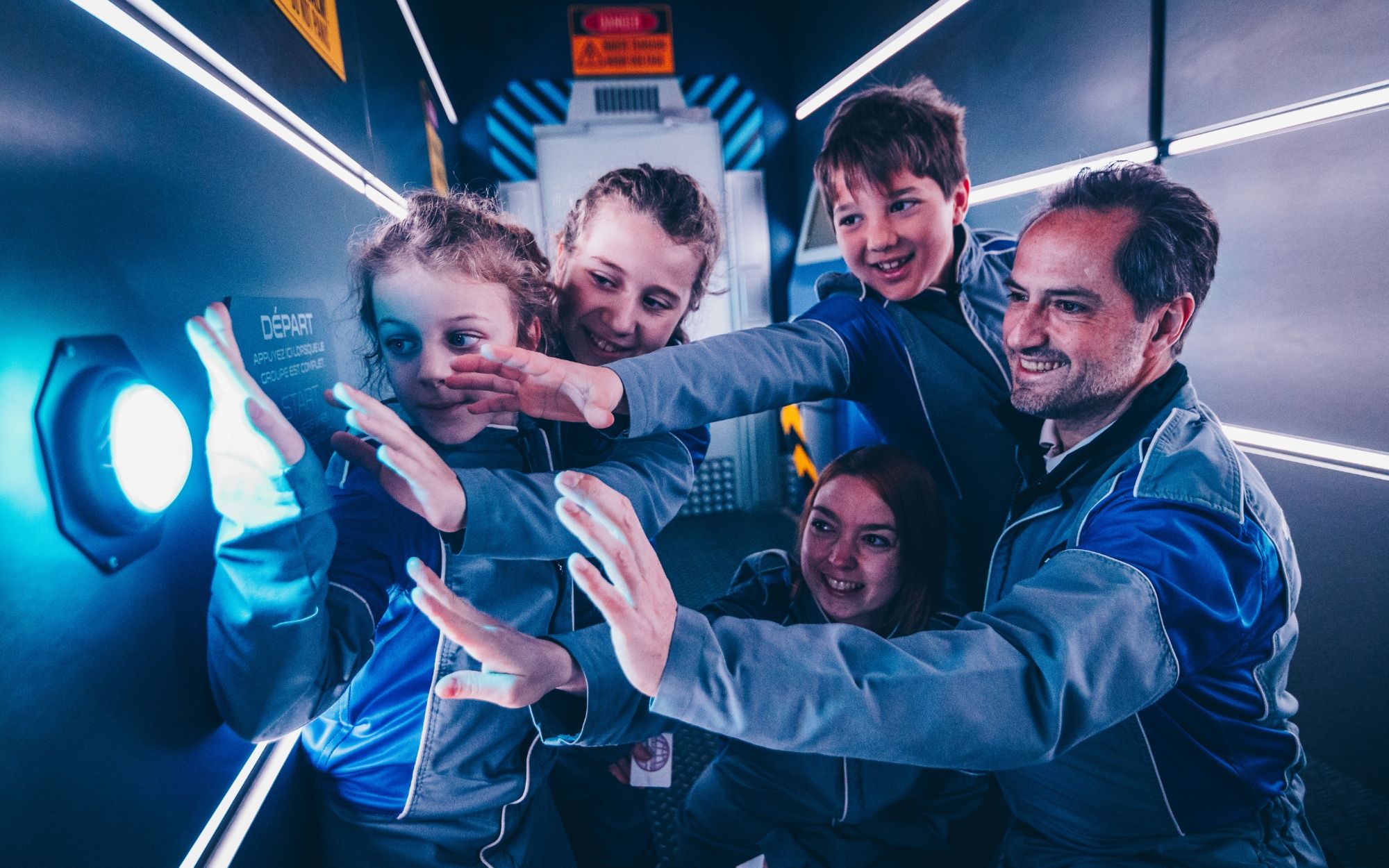 Famille à l'escape game en combinaisons bleues souriants