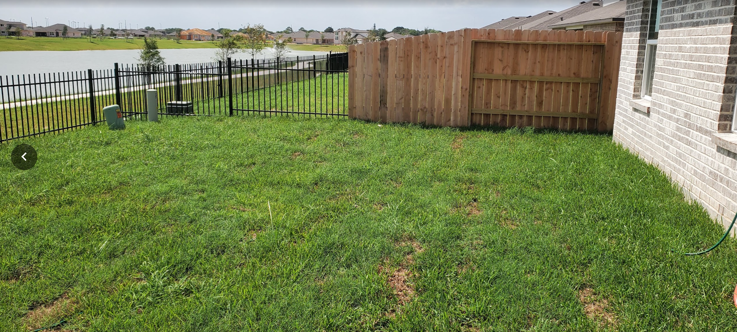 Wide view of backyard before outdoor living renovation with existing grass lawn and lakefront fence