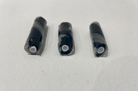 Three short black glass rods lying in a row, each cut to reveal a small white core ringed by fine concentric layers.