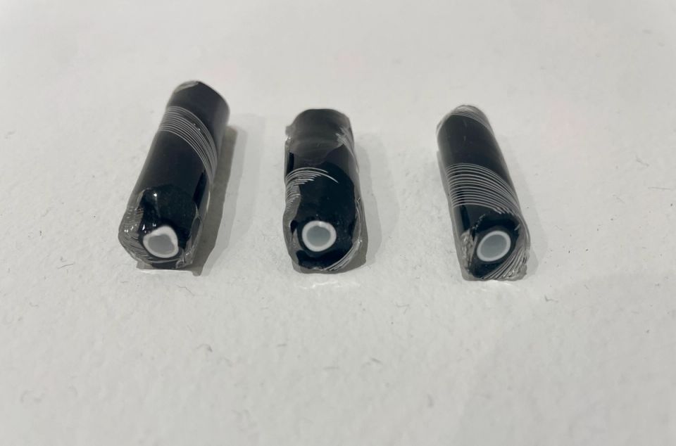 Three short black glass rods lying in a row, each cut to reveal a small white core ringed by fine concentric layers.