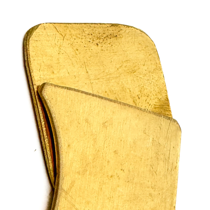 A close view of two brass pieces overlapping, the surface scratched and dented and the thin gauge of the metal visible along the cut edge.