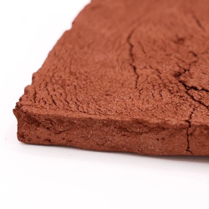 A close view of the slab's corner, its brick-orange surface cracked and grainy above a thick, coarse edge.