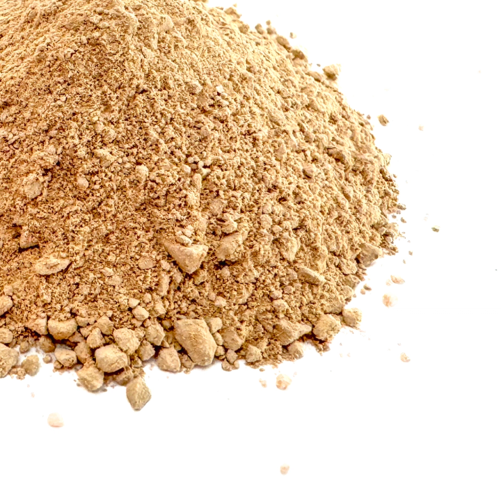 A close view of the powder heaped high, the grains coarse and lumpy in warm sandy tan with fines spilling at the base.