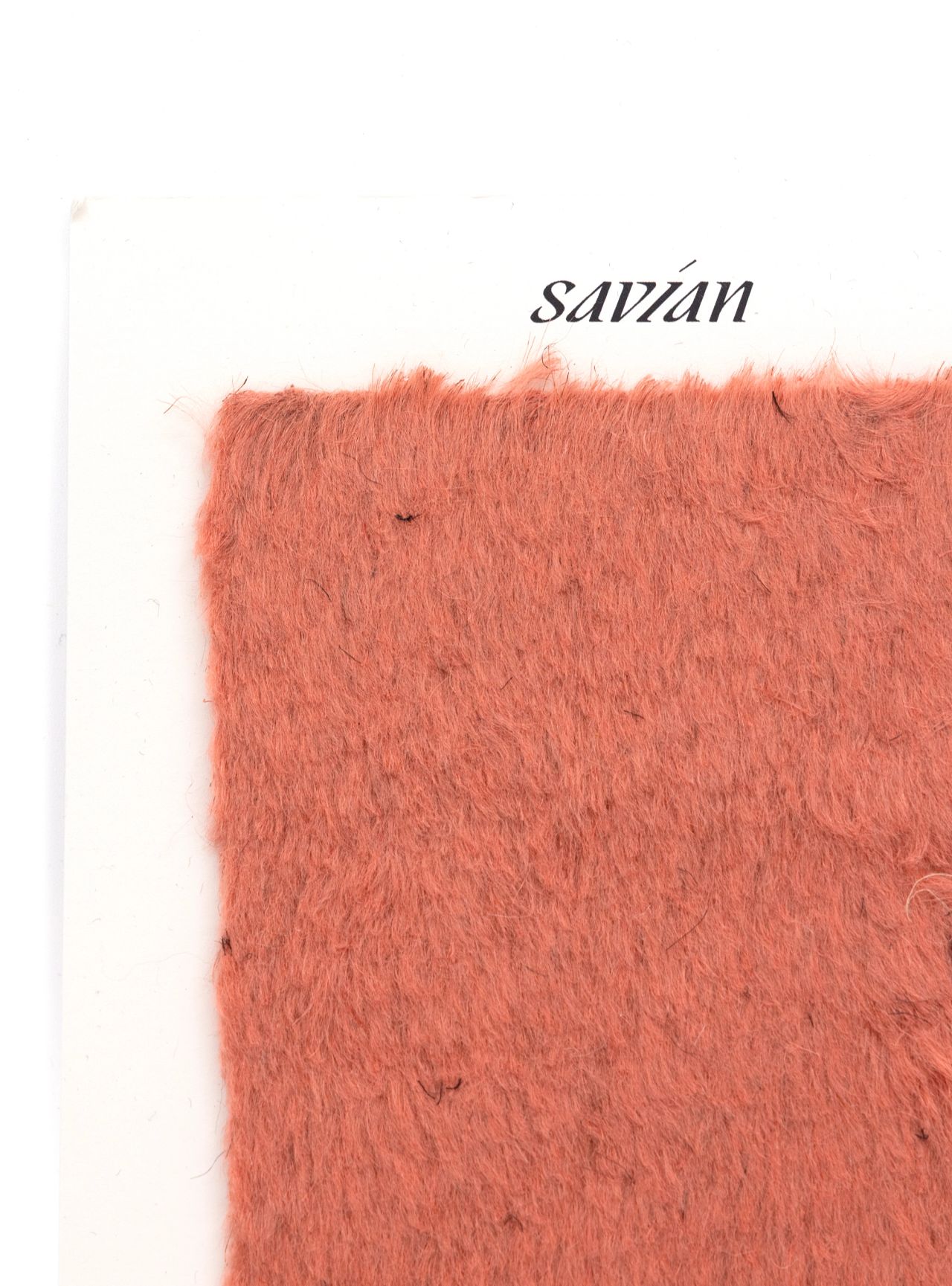 A square of dense coral-orange pile fur mounted on a white card printed “savian”, the fibres soft and slightly matted.