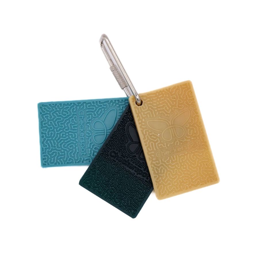 Three rectangular sample chips clipped to a steel carabiner in teal, deep green and mustard, each moulded with a dense maze-like relief pattern and stamped with the Checkerspot name and butterfly mark.