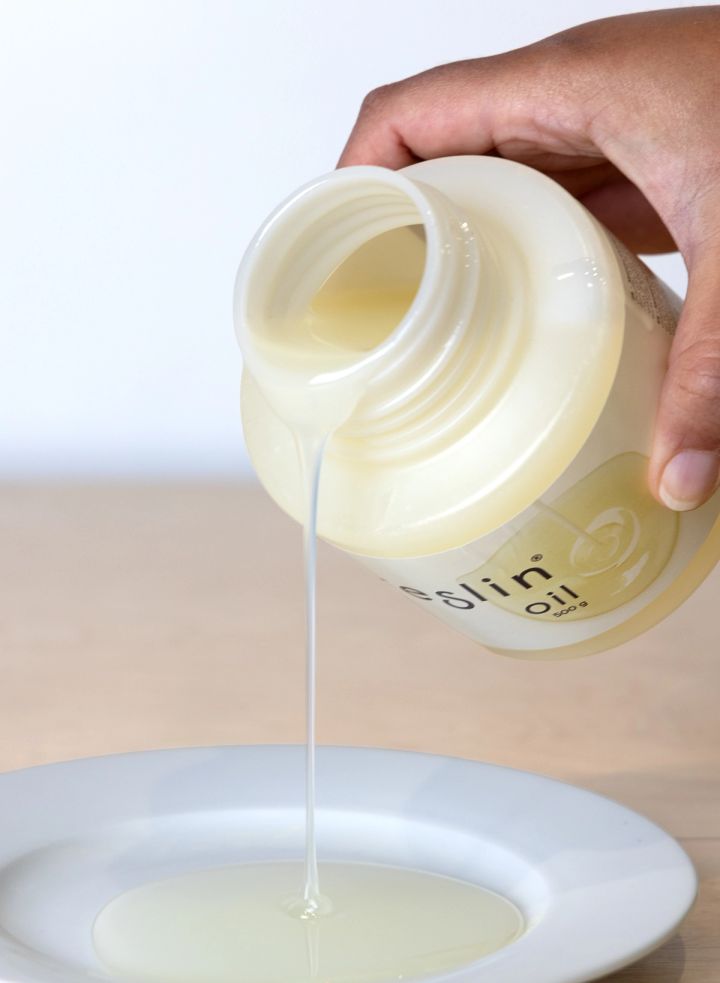 A hand tipping the tub so the pale yellow resin pours in a slow thread onto a white dish, showing how it flows.