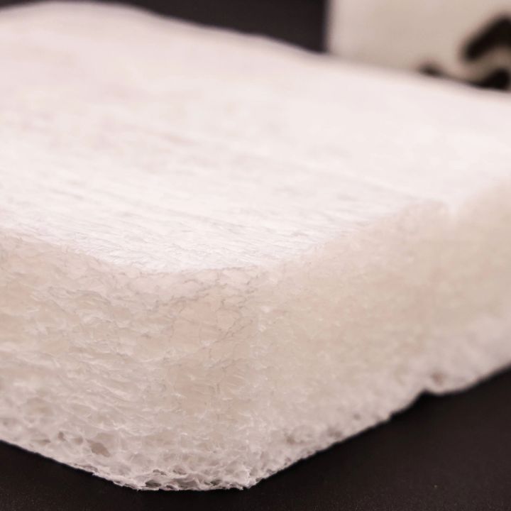 The slab seen close along its cut edge, the open cell structure and fibrous interior visible where the foam has been sliced.