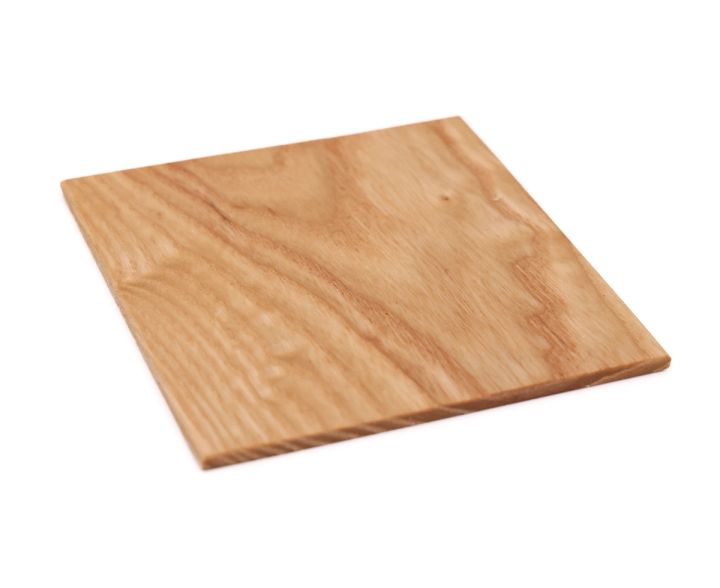 The same square tilted at an angle, its planed face catching the light and the thin cut edge visible below.