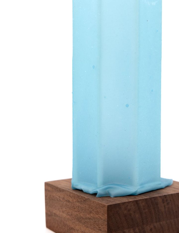 A close view of the aqua column on its walnut base, the faceted sides and the pooled, rippling foot filling the frame.